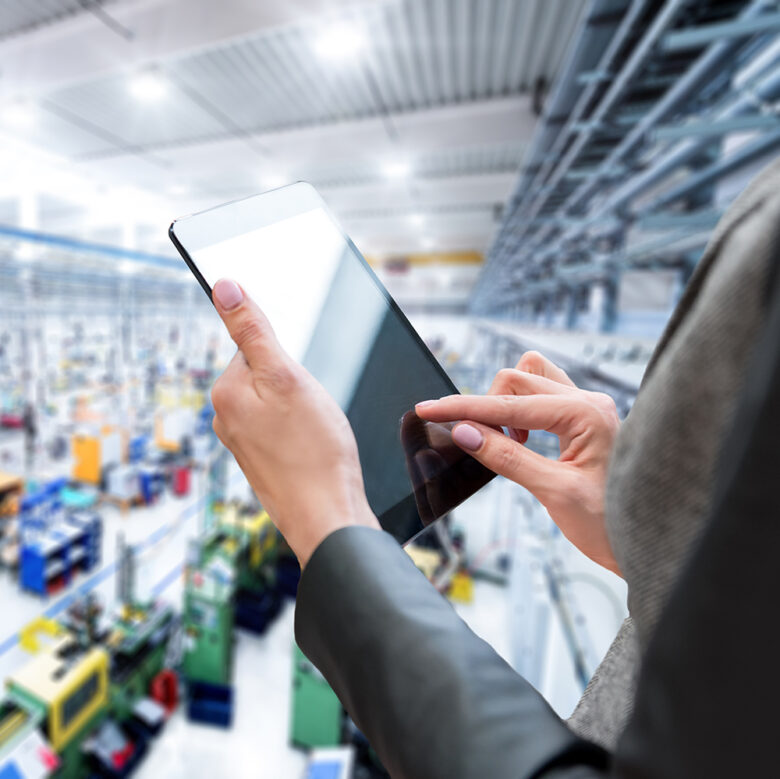 Female manager & tablet in new factory Horizontal color image of businesswoman - unrecognizable person - working with digital tablet in large futuristic factory. Woman standing on top of a balcony, holding touchpad and checking inventory of a manufacturing company on touchscreen tablet. Focus on businesswoman's hands holding black tablet, futuristic machines in background.
