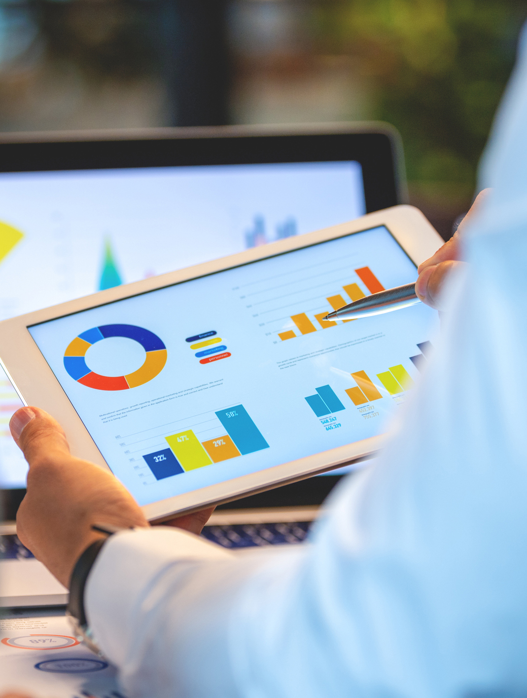 Two business men working on a laptop and digital tablet with financial charts, graphs and data in the office Two business men working on a laptop and digital tablet with financial charts, graphs and data in the office. There is also paperwork with accounting data